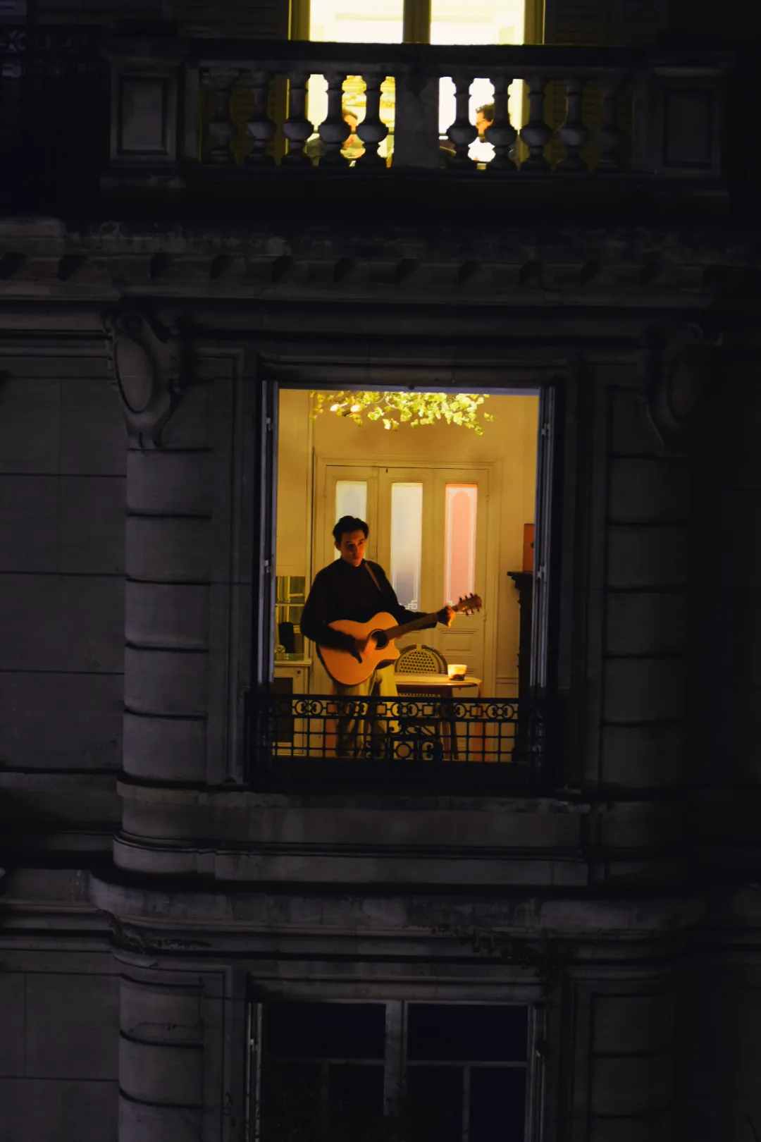 Imran joue de la guitare dans l’encadrement de sa fenêtre, la nuit