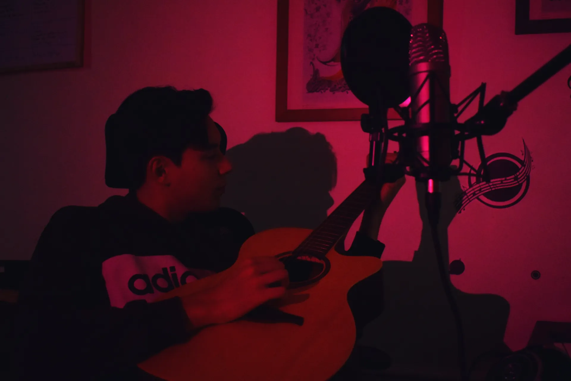 Imran à la guitare devant le micro, studio baigné de rose
